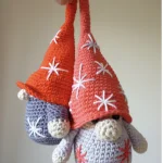 Two hand-crocheted Little Fino Gnome Amigurumi dolls with red hats and star patterns are held by one hand, with the text 